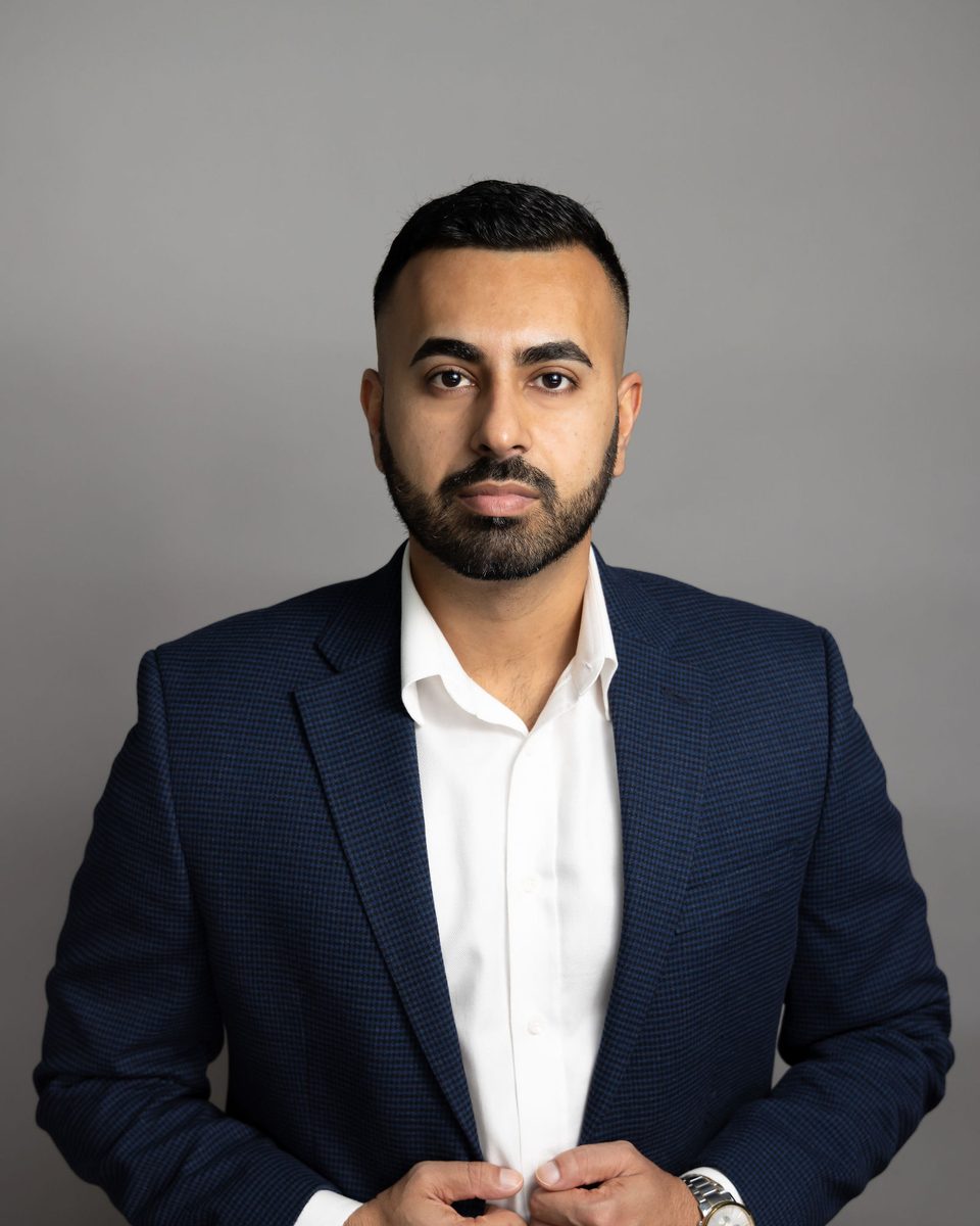 Editorial portrait of a man in a navy blazer buttoning his jacket against a gray backdrop, photographed by TM Headshots