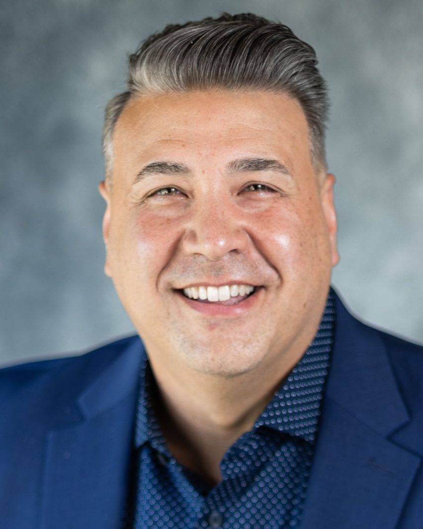 Headshot of a smiling man in a blue blazer against a gray painted canvas backdrop, photographed by TM Headshots